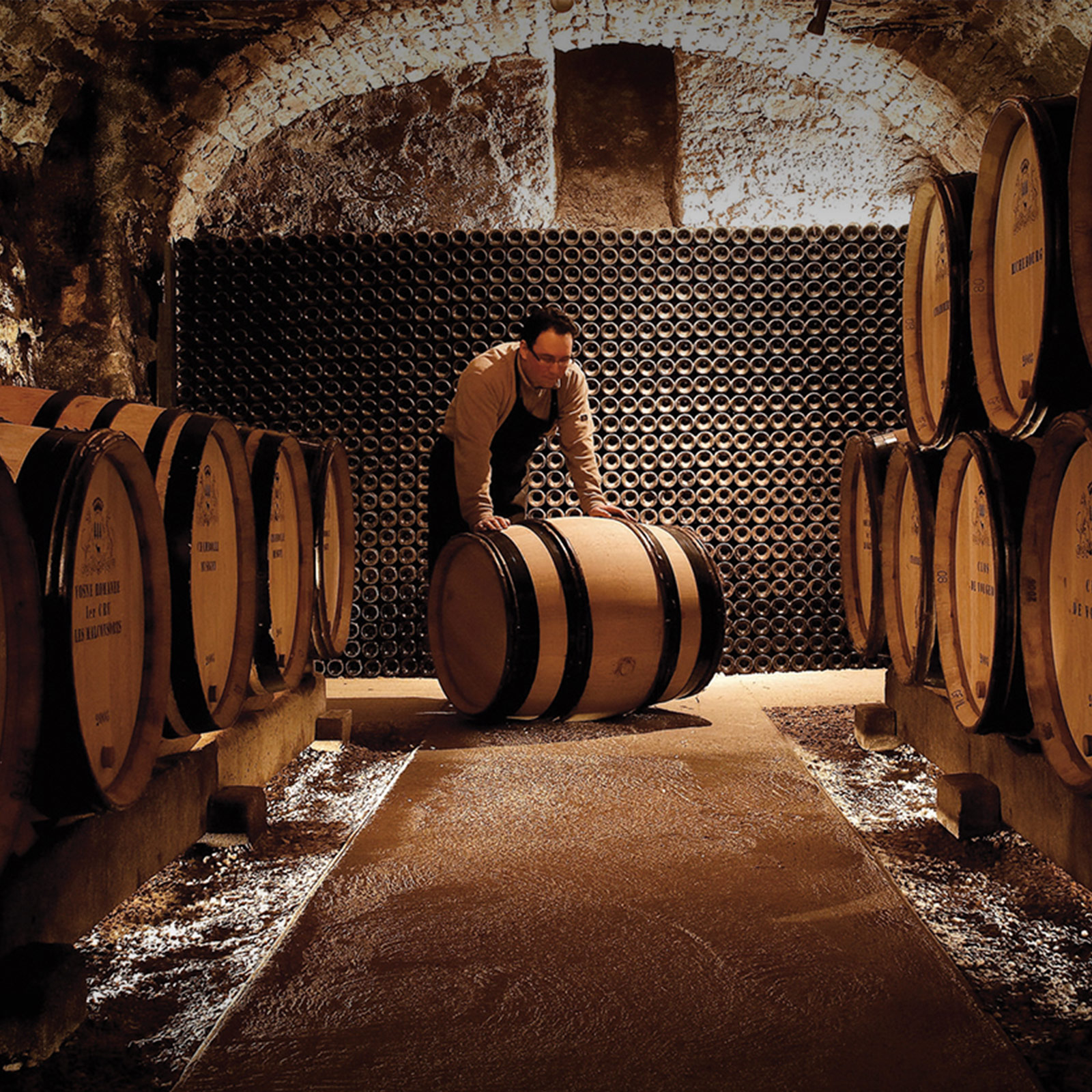 Vintner in a wine cellar rolling a wine barrel